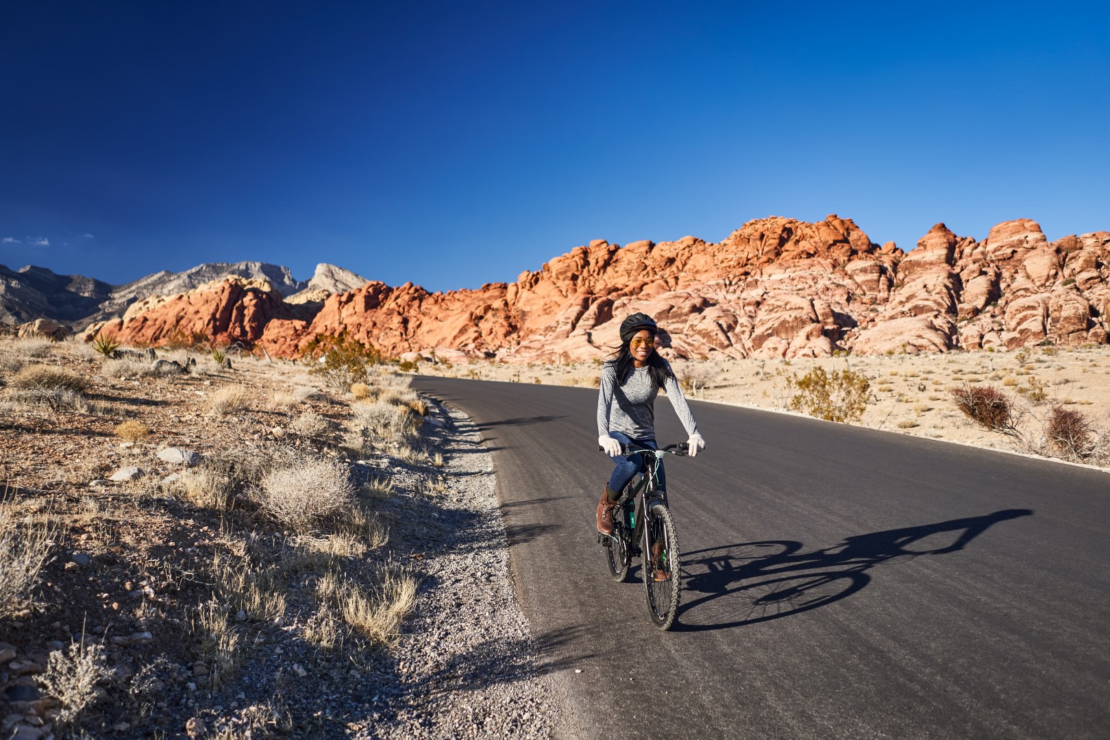 Woman biking near Red Rock Canyon against red rock formations and blue sky in Las Vegas, NV.