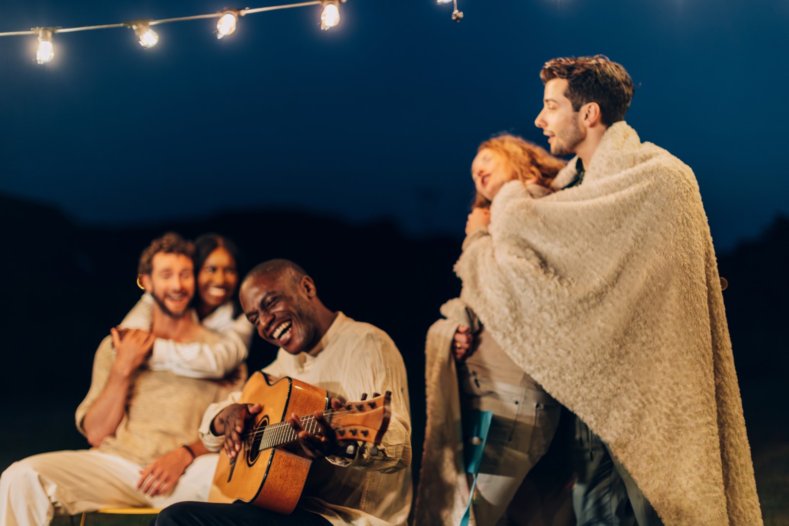 Friends gathered at Red Rock RV Resort, enjoying an evening with a guitar and blankets under string lights.